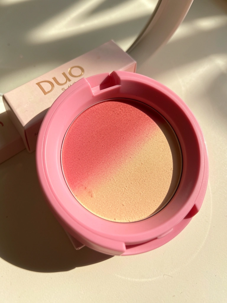 Estojo de blush duo rosa e pêssego sobre superfície clara, textura rica e gradiente de cor visível, luz natural difusa com reflexo sutil.