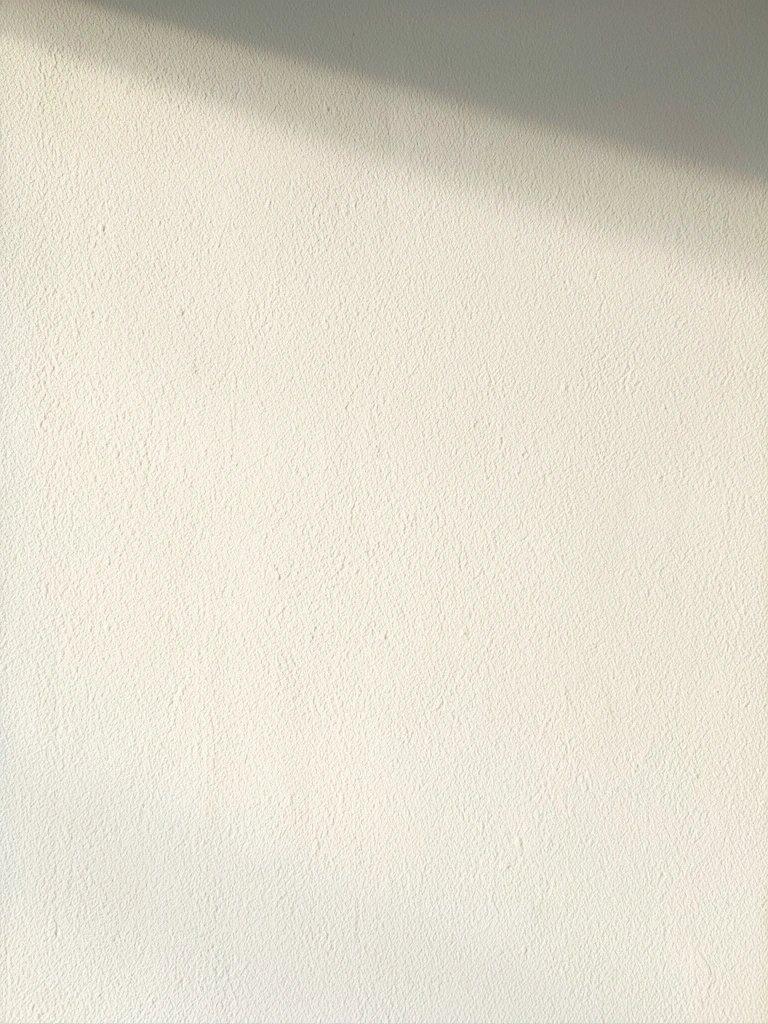 Parede branca com textura fina e aveludada, iluminada por luz natural que realça suas nuances suaves e sombras delicadas.
