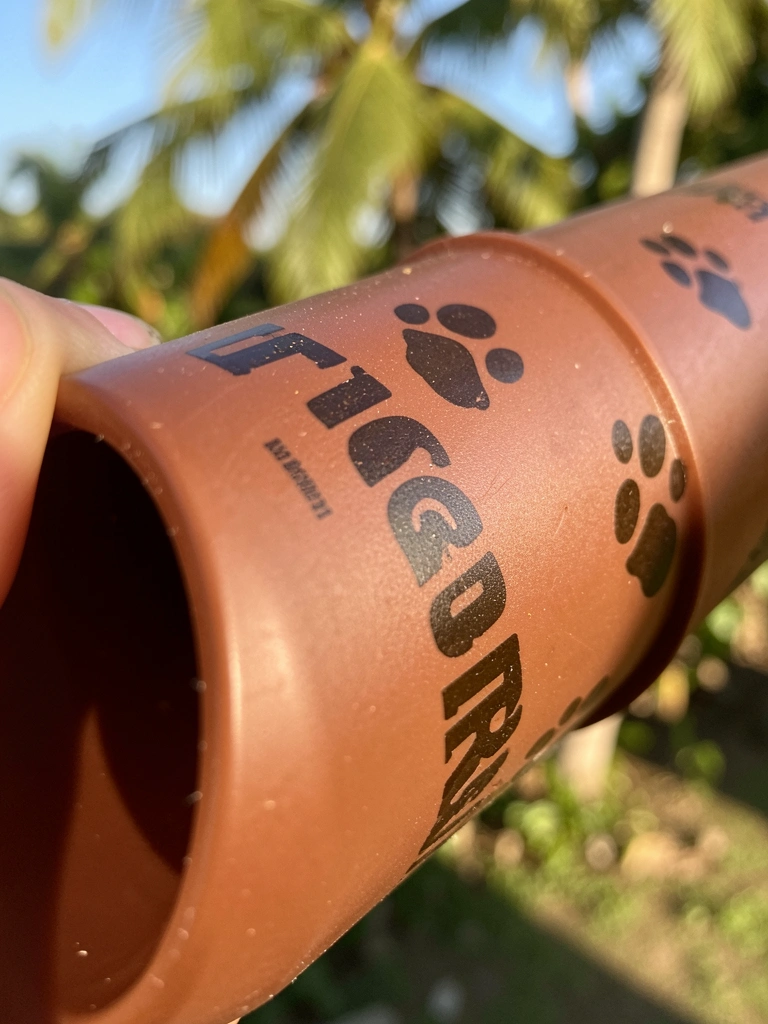 Canos de plástico marrom com decalques de pegadas de cachorro da TIGRE, textura fosca e luz natural tropical.