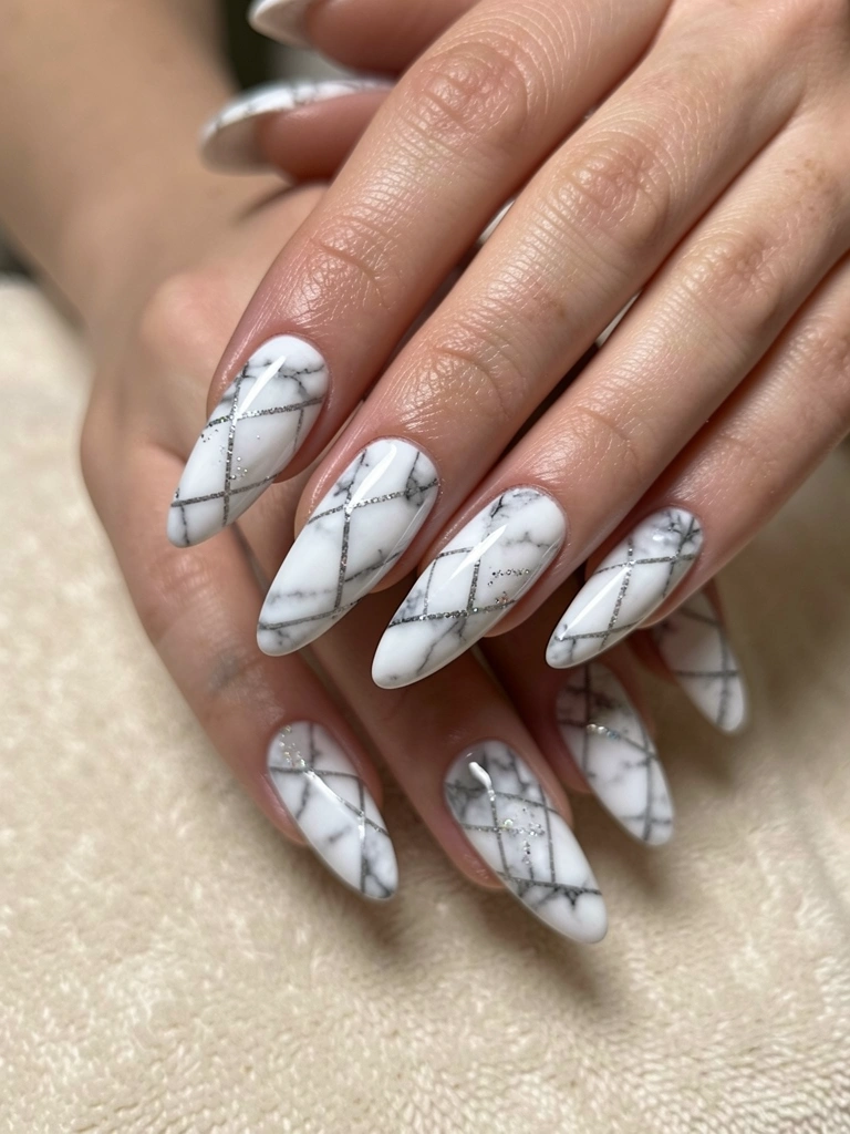 Mãos com unhas longas e brilho fosco, padrões geométricos em mármore cinza e branco com glitter sutil, iluminação difusa e fundo neutro.