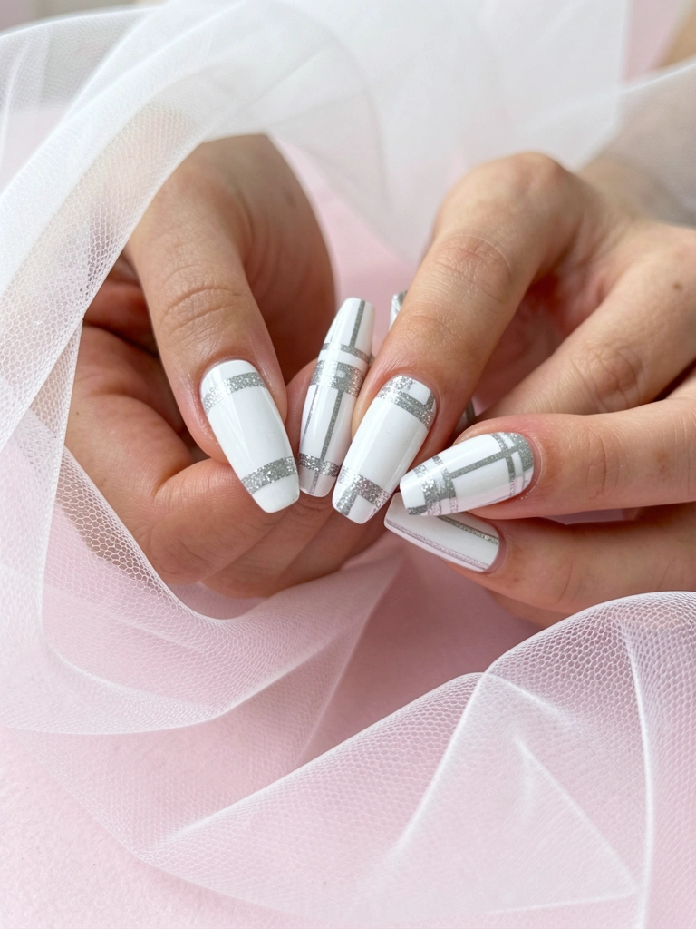 Mãos seguindo unhas compridas em formato bailarina com listras brancas e prateadas e glitter, sobre superfície rosa clara e tule branco esvoaçante ao fundo.