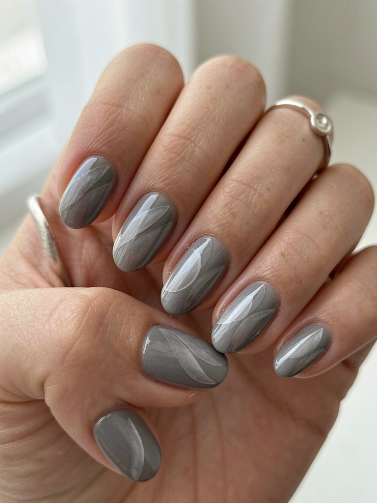 Mãos femininas com unhas em esmalte cinza ombré e padrão olho de gato, anel de prata, luz natural difusa e fundo desfocado.