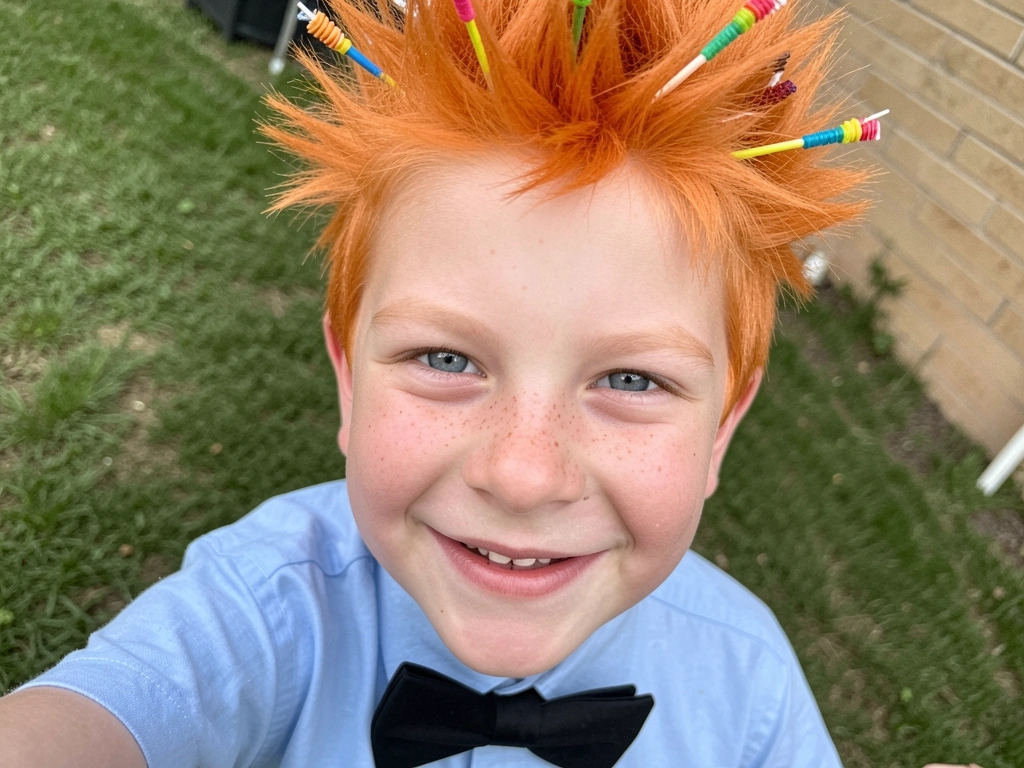 Menino com cabelo curto espetado para cima, decorado com palitos de dente coloridos, sorrindo.