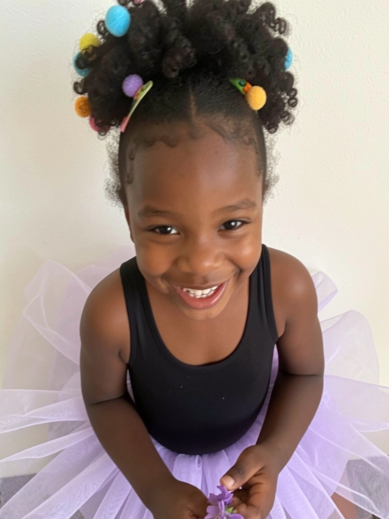 Menina negra sorrindo com cabelo crespo decorado com pompons coloridos presos em molas.