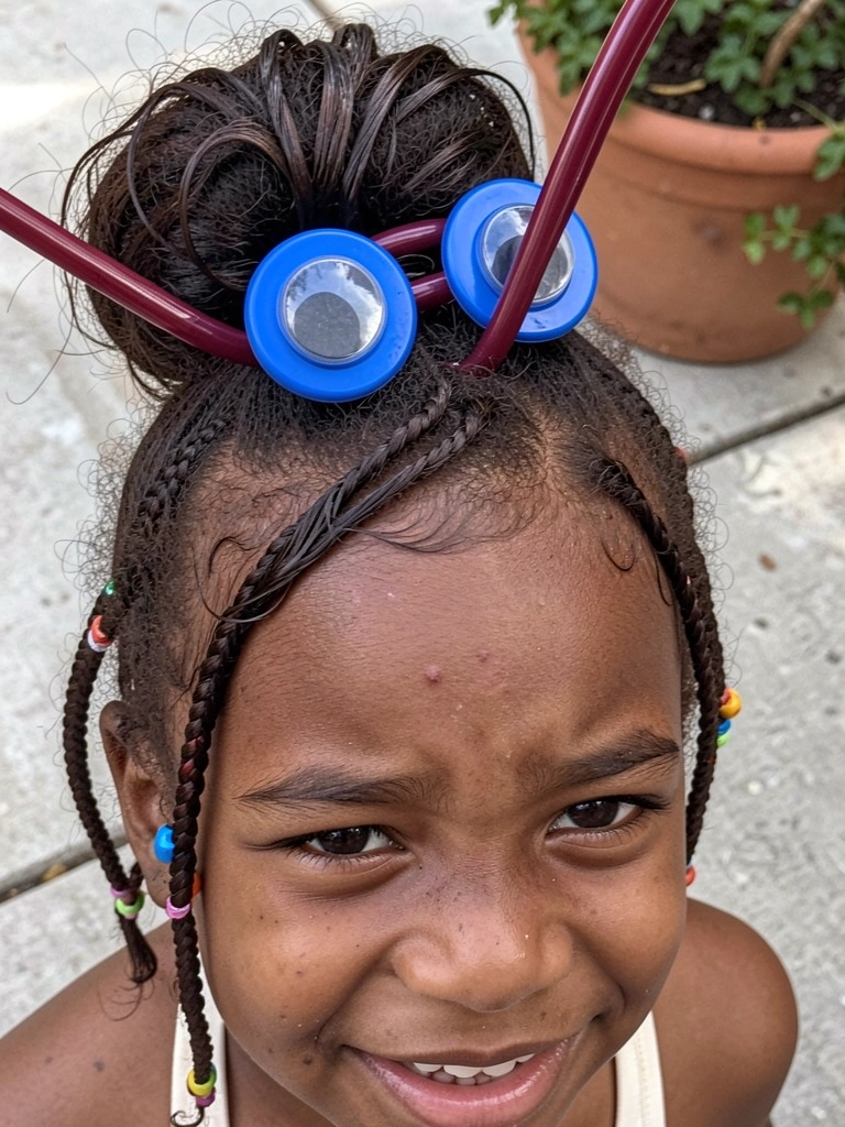 Menina negra com tranças finas decoradas com miçangas coloridas, olhando para cima.
