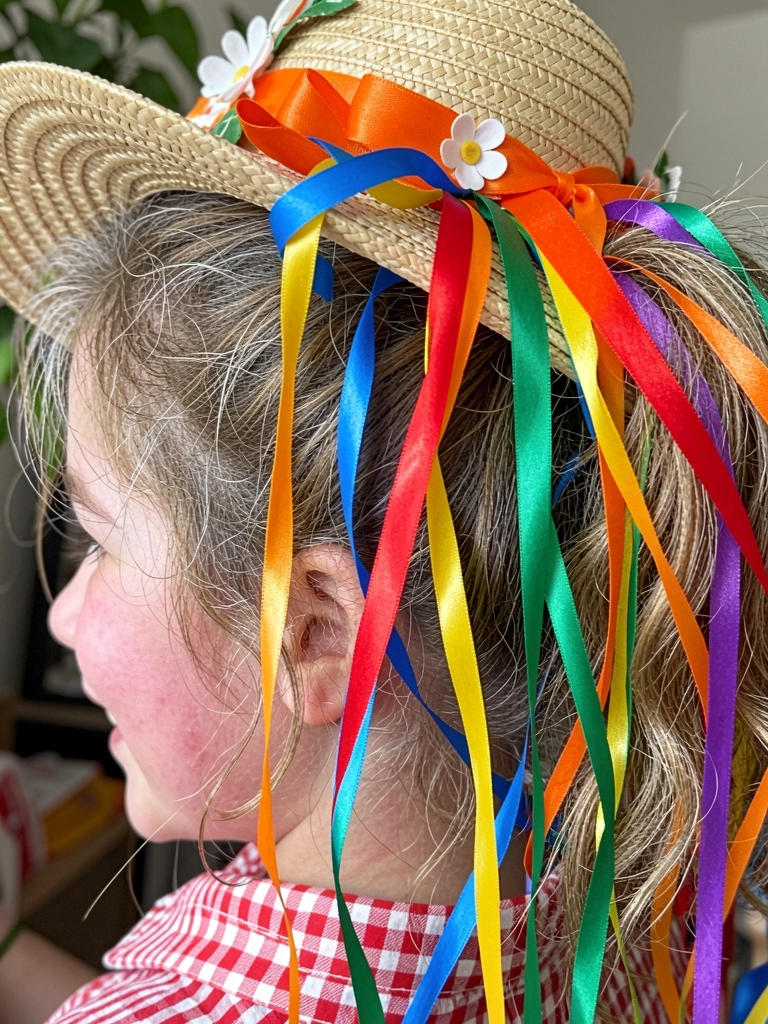 Acessórios de festa junina: minichapéu de palha, bandeirinhas coloridas, fitas xadrez e laços de chita sobre superfície de madeira.
