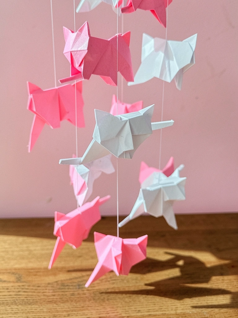 Móbile suspenso com dobraduras de papel rosa e branco em formato de gato.