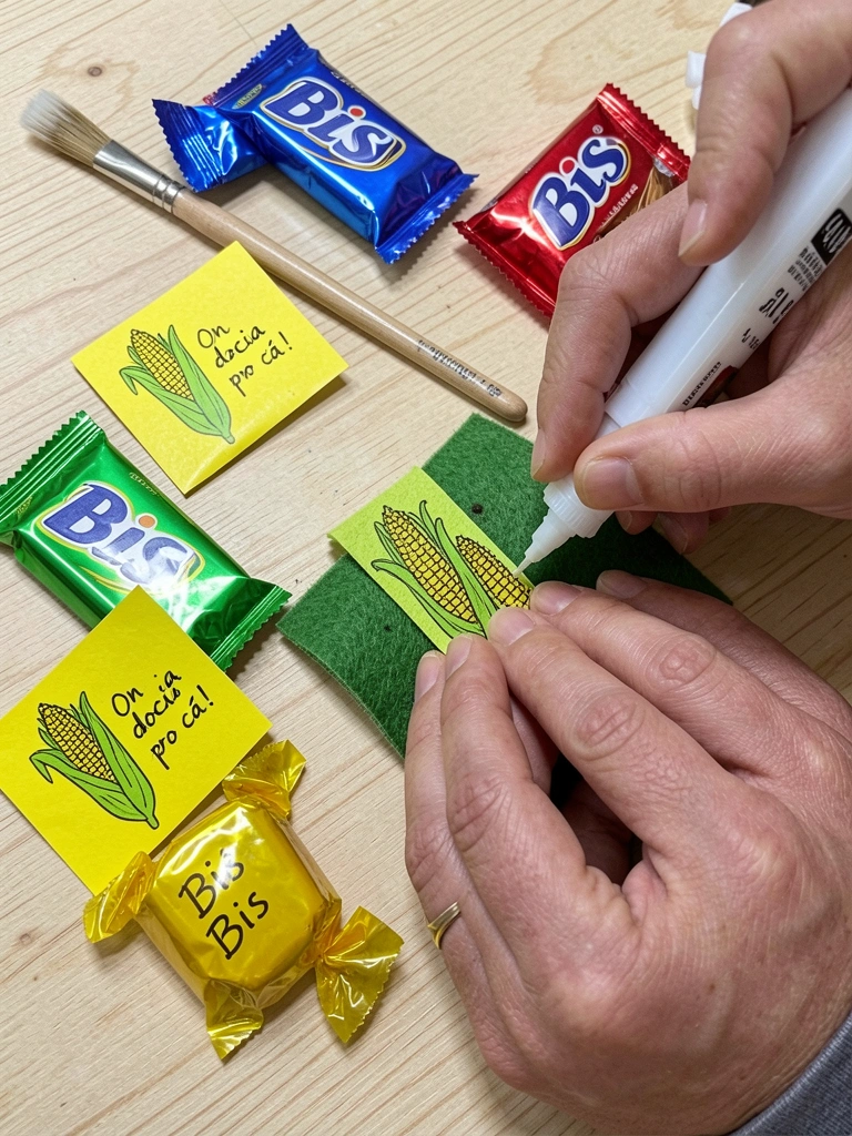 Mãos aplicam cola quente em fita de chita sobre feltro, pincel ao lado.