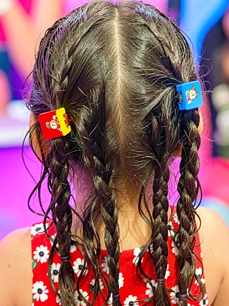 Criança de cabelo curto usando tiara com fitas e bandeirinhas, sorrindo amplamente.
