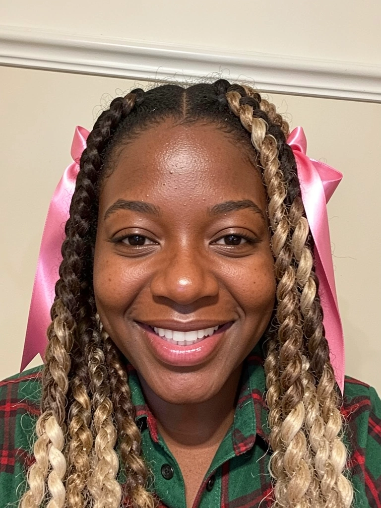 Close-up de rosto com duas tranças boxeadoras em cabelo crespo, fitas vermelhas e amarelas entrelaçadas.