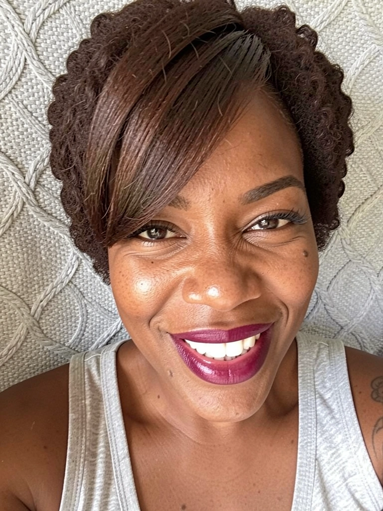 Mulher negra com cabelo cacheado curto desfiado e franja lateral, sorrindo.