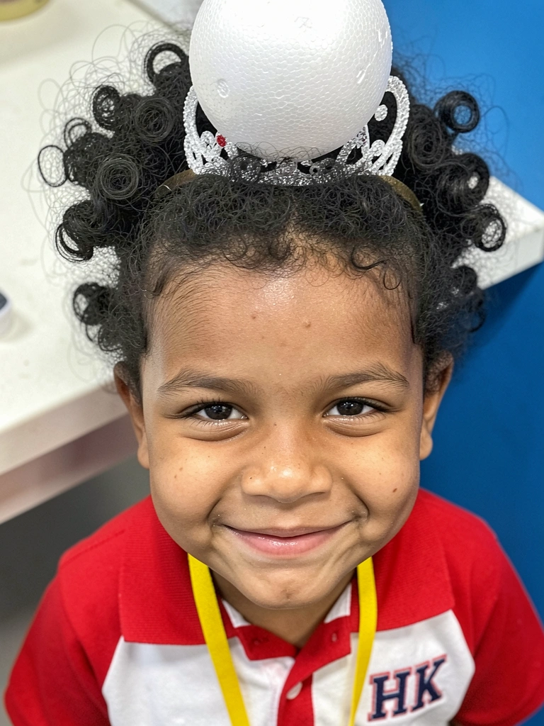 Criança com cabelo cacheado modelado como sorvete, usando tiara com bola de isopor.