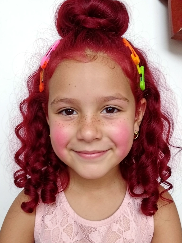 Menina com cabelo cacheado preso em meia bola com fios soltos nas laterais.