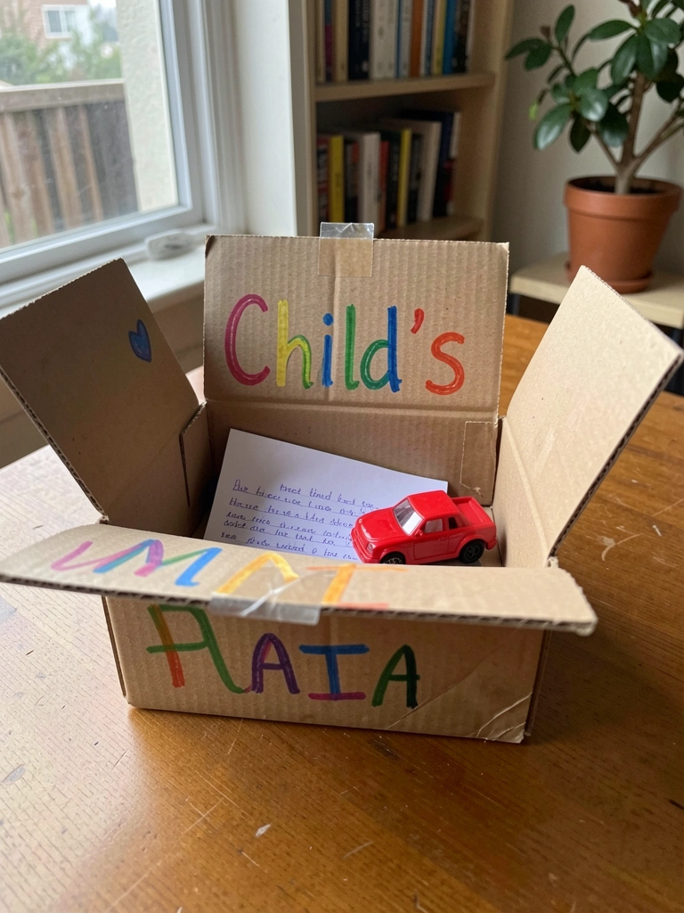 Caixa de papelão personalizada com nome de criança, contendo um bilhete e um pequeno brinquedo.