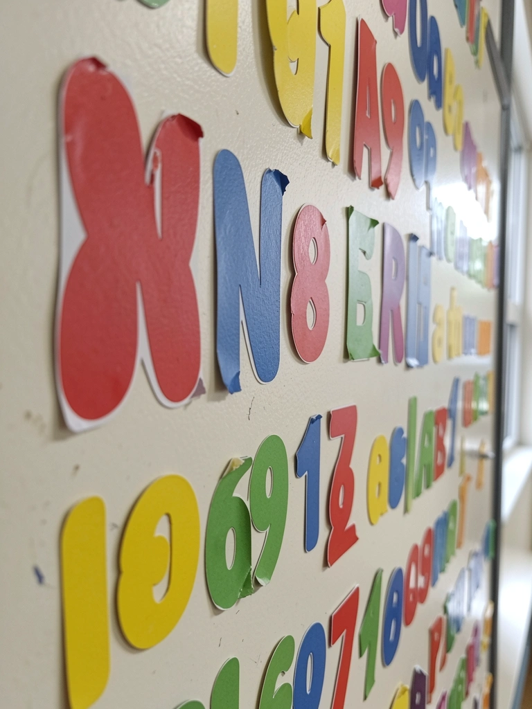 Parede de sala de aula com adesivos coloridos de letras e números.