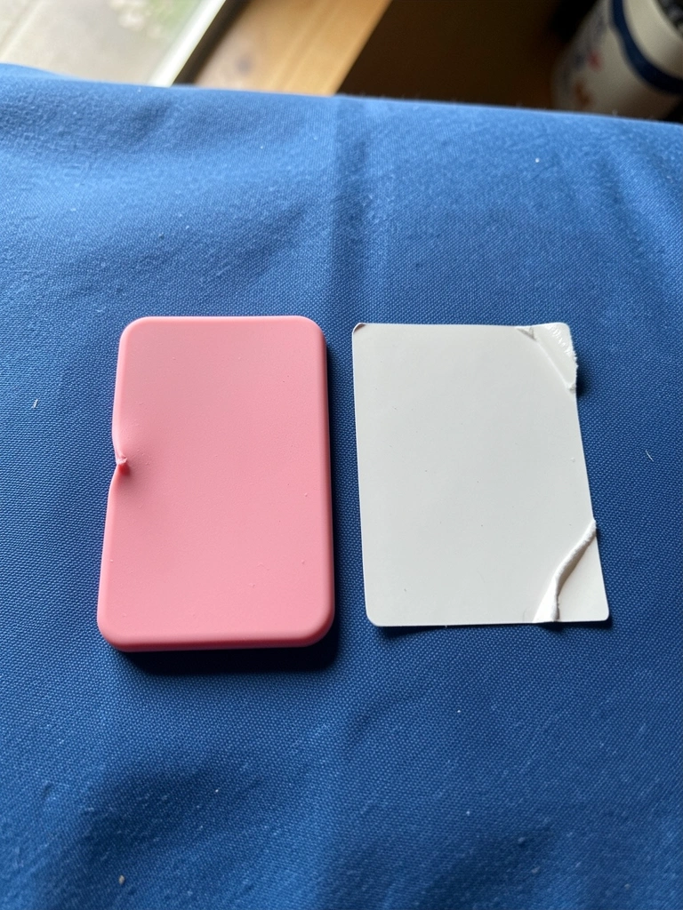 Duas etiquetas lado a lado sobre tecido azul: uma de silicone rosa e outra adesiva branca.