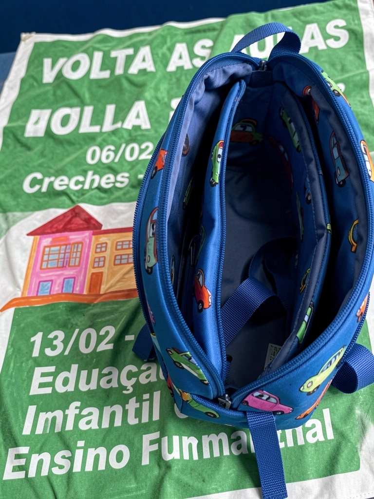 Mochila azul com estampa de carrinho, aberta, exibindo compartimentos internos e alças.
