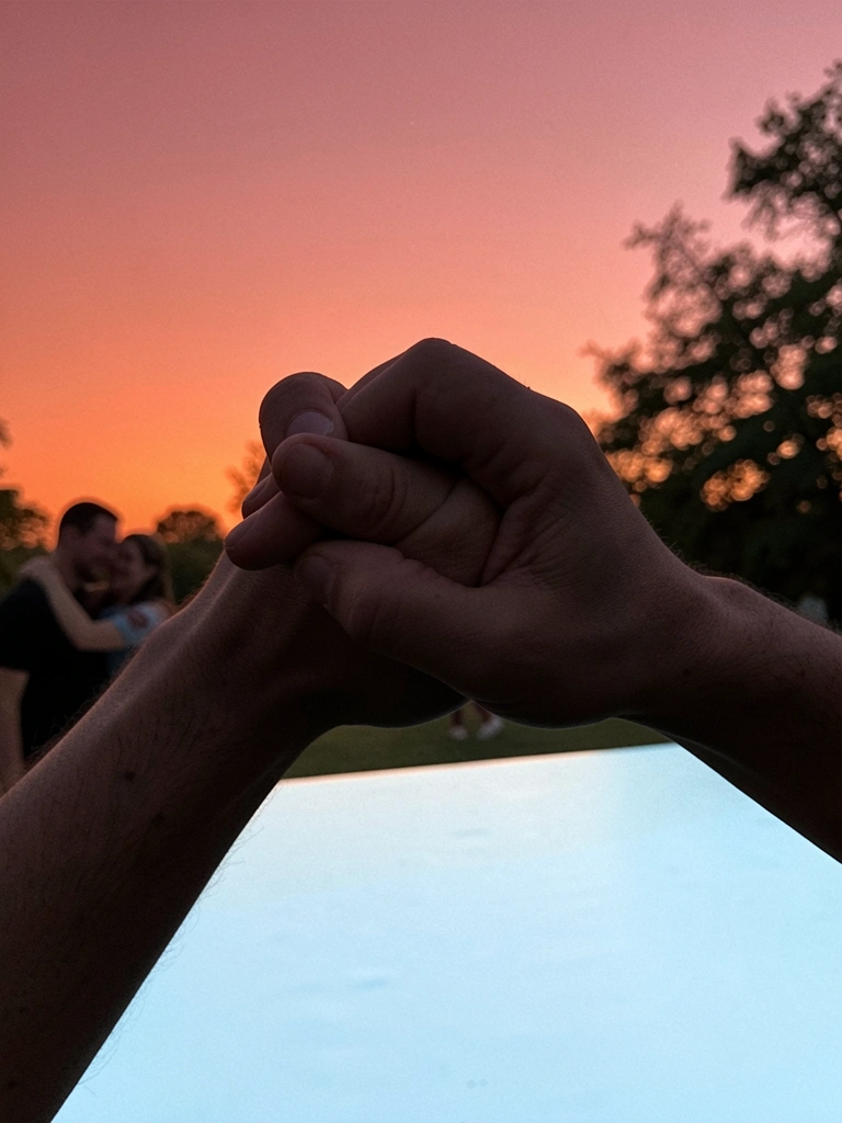 Casal abraçado em um parque, sorrindo, com árvores ao fundo e luz do entardecer.