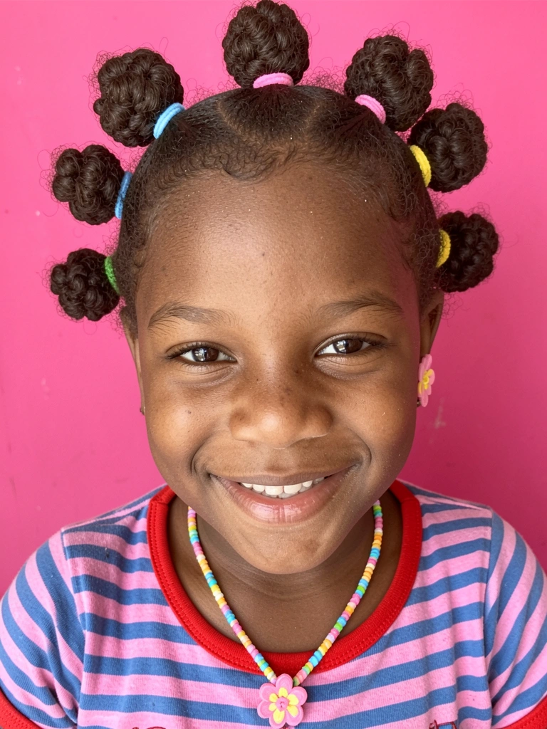 Cabelo cacheado dividido em várias bantu knots presas com elásticos coloridos.