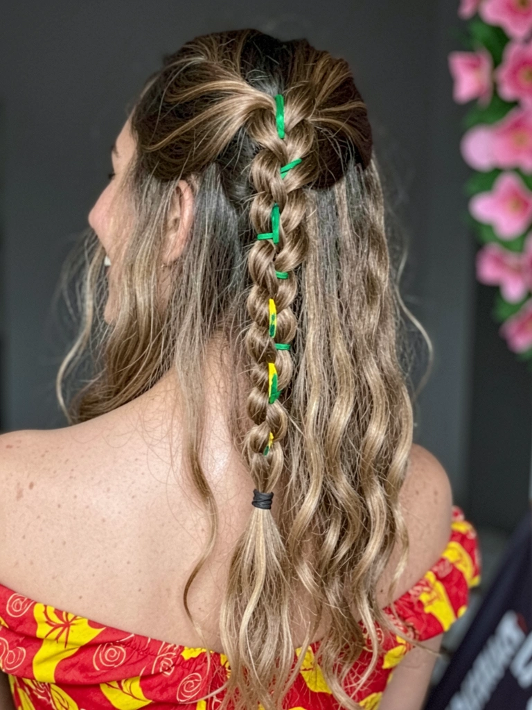 Cabelo dividido ao meio com duas marias-chiquinhas presas com elásticos verde e amarelo.