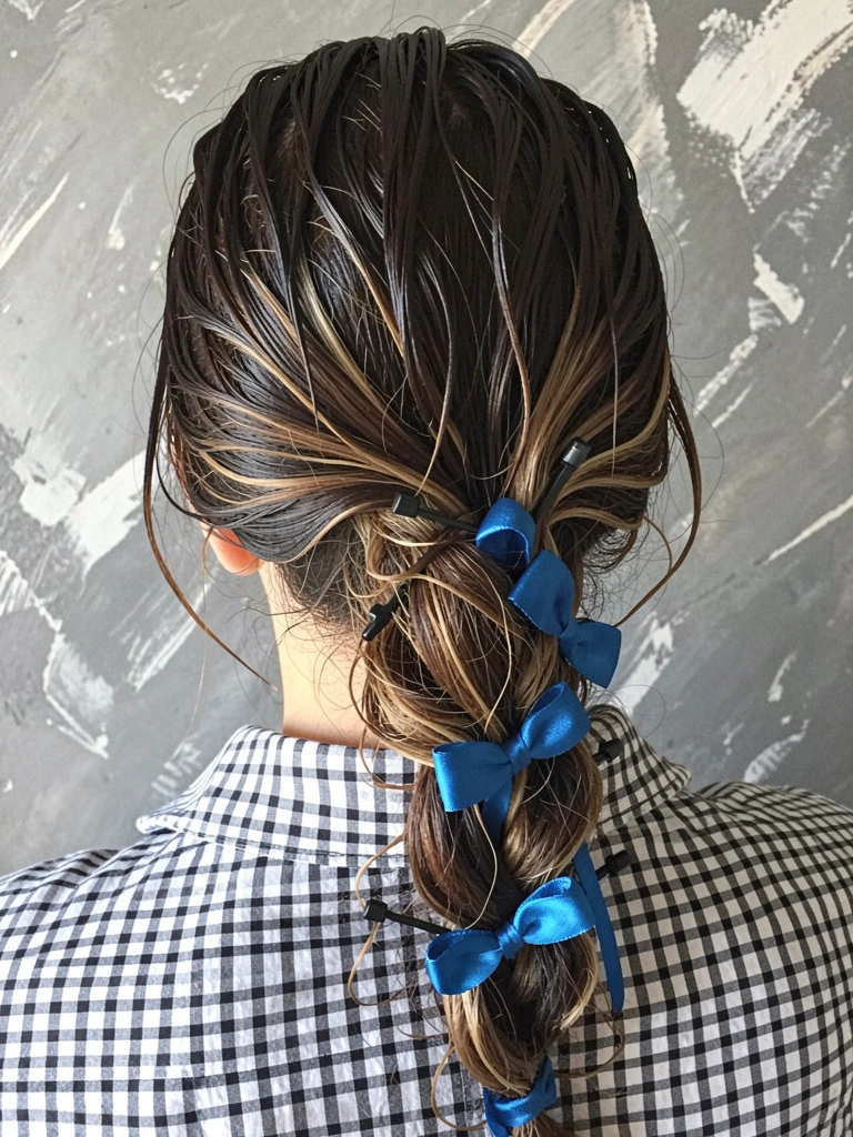 Mãos trançando cabelo com fita de cetim azul, passo a passo.