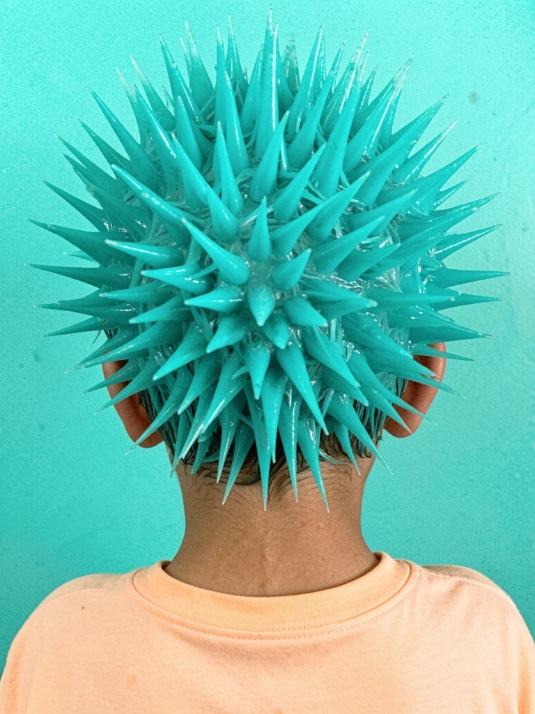 Menino com cabelo espetado e gel colorido, sorrindo para a câmera.