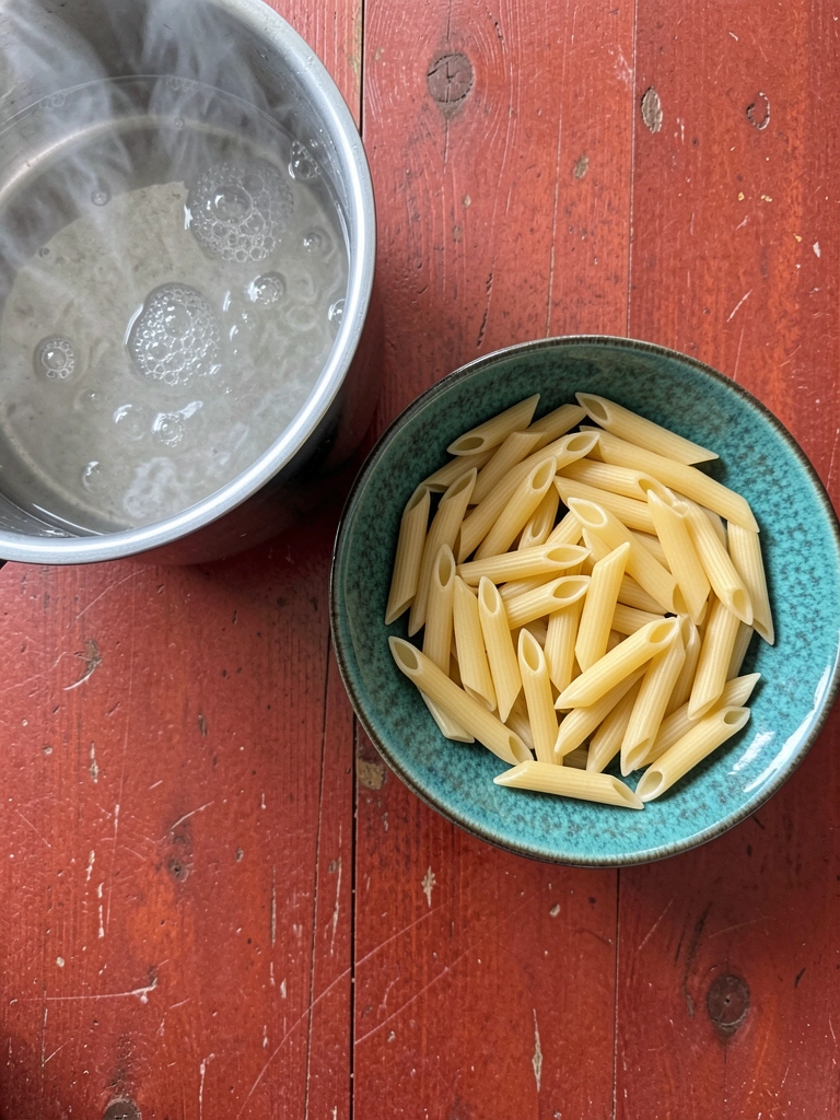 Macarrão penne seco e água fervente em uma panela.